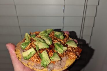 Una tostada con frijoles, tinga de pollo, y aguacate
