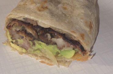 Un burrito de arrachera y mollejas con cebollas asadas, queso oaxaca flameado, y aguacate