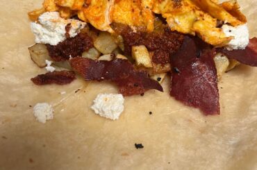 Burrito de desayuno con papas y chorizo, tocino de pavo y huevos y salsa roja y queso fresco.