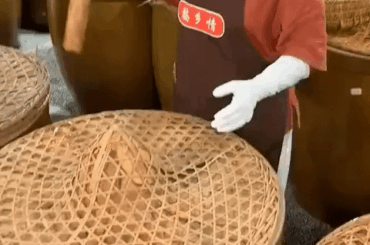 This woman opening a barrel of fermenting peppers, with a garlic topping.