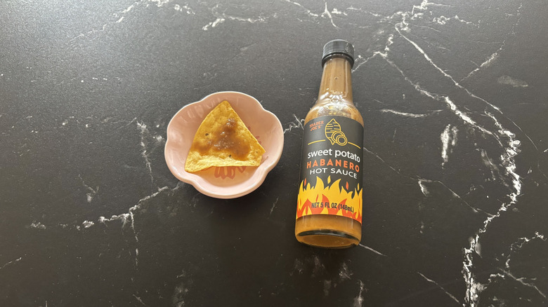 Trader Joe's sweet potato habanero hot sauce bottle next to tortilla chip on small plate with drizzle of sauce