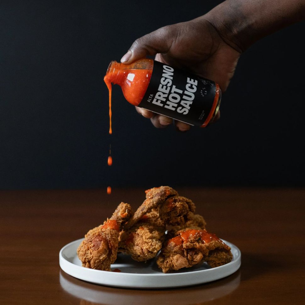 A bottle of Alta hot sauce being poured over a plate of fried chicken wings.