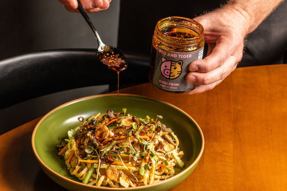 Pig and Tiger Chili Crisp being spooned onto a plate of noodles and vegetables.