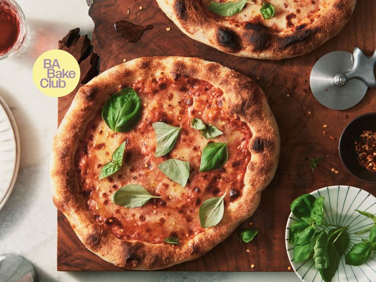 Two whole cheese pizze topped with red pepper flakes olive oil and basil leaves on a wooden cutting board.