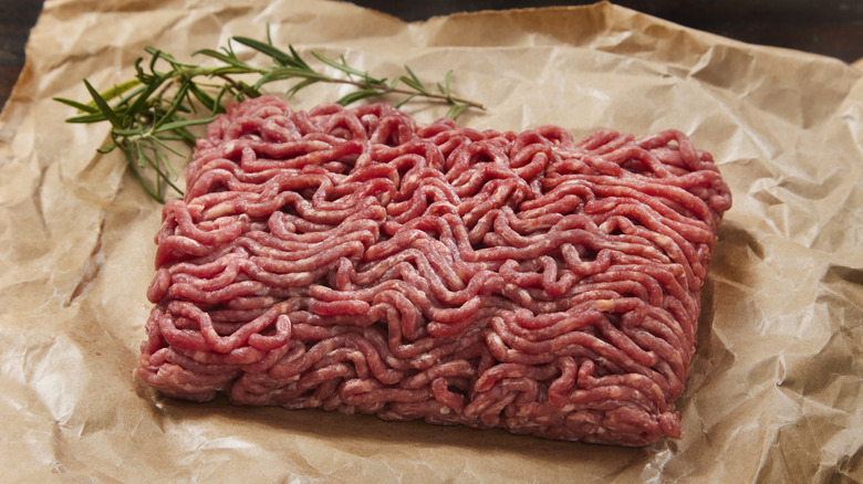 Raw ground beef on parchment paper with sprig of rosemary