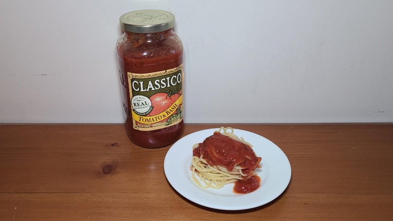 Jar of Classico pasta sauce with a small white plate of spaghetti topped with sauce