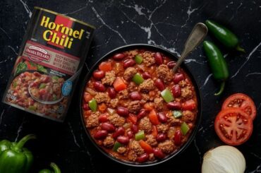 HORMEL® Chili & OMAHA STEAKS® 100% Natural Beef Chili with Beans can next to bowl full of HORMEL® Chili & OMAHA STEAKS® 100% Natural Beef Chili with Beans. A peppers, onion, and tomatoes surround the product.