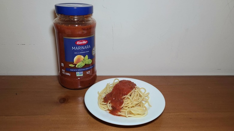 Jar of Barilla pasta sauce with a small white plate of spaghetti topped with sauce