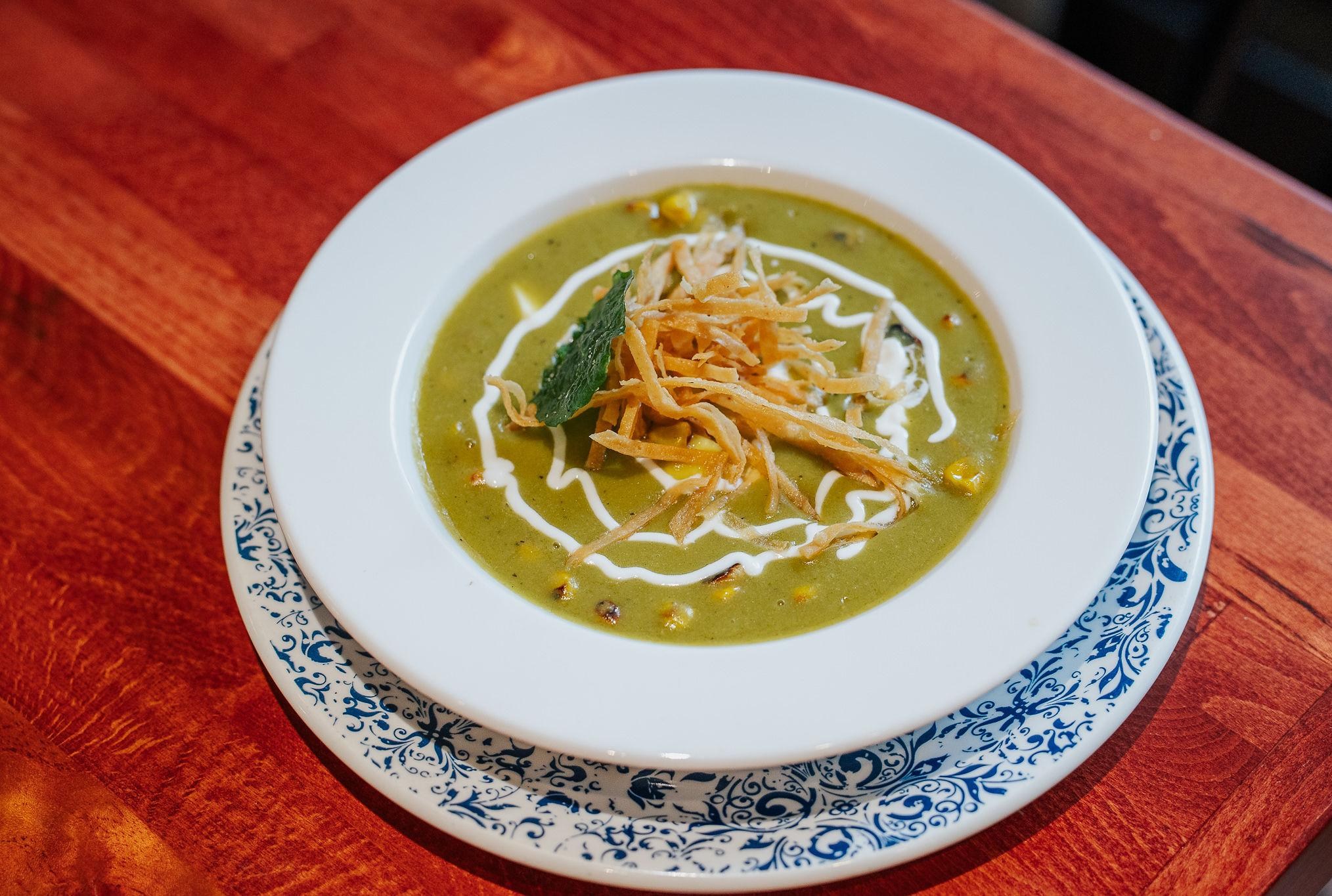 A bowl of creamy poblano soup with crispy tortilla shreds.