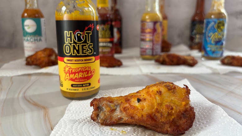 Bottle of Hot Ones Tropical Amarillo hot sauce on table next to chicken wing