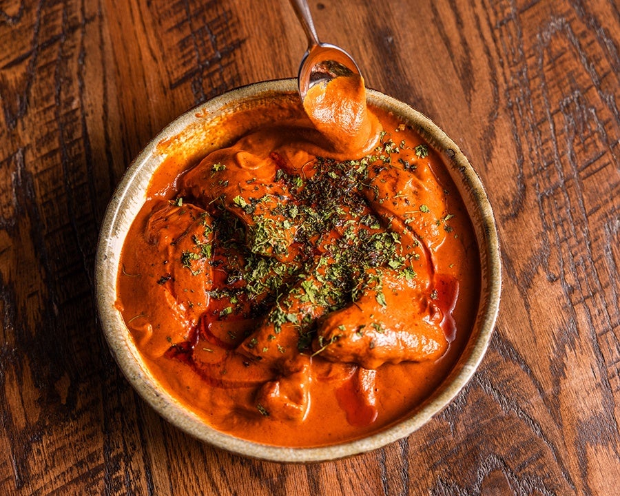 Overhead view of a spoon dipping into a thick, bright orange Indian curry.