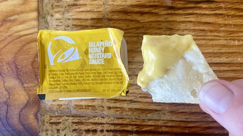Hand holding tortilla chip dipped in Taco Bell Jalapeño Honey Mustard Dip Sauce