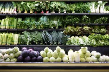 A display of various fresh green vegetables including lettuce, kale, and celery in a grocery store.