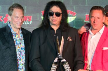 Gene Simmons holding big scissors, with the co-owners next to him