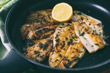 Cooked flounder fillets garnished with herbs and a lemon slice in a frying pan.