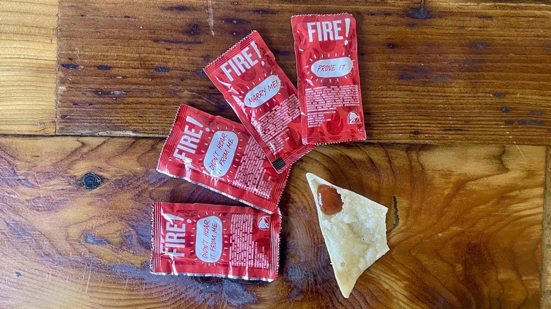 Packets of Taco Bell Fire Sauce with a dollop of it on a tortilla chip