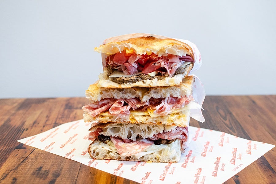 A stack of three meat-and-cheese-filled sandwiches on Tuscan flatbread, which looks like a thinner focaccia.
