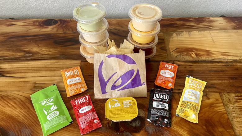 Packets and ramekins of Taco Bell sauces with a small bag of tortilla chips