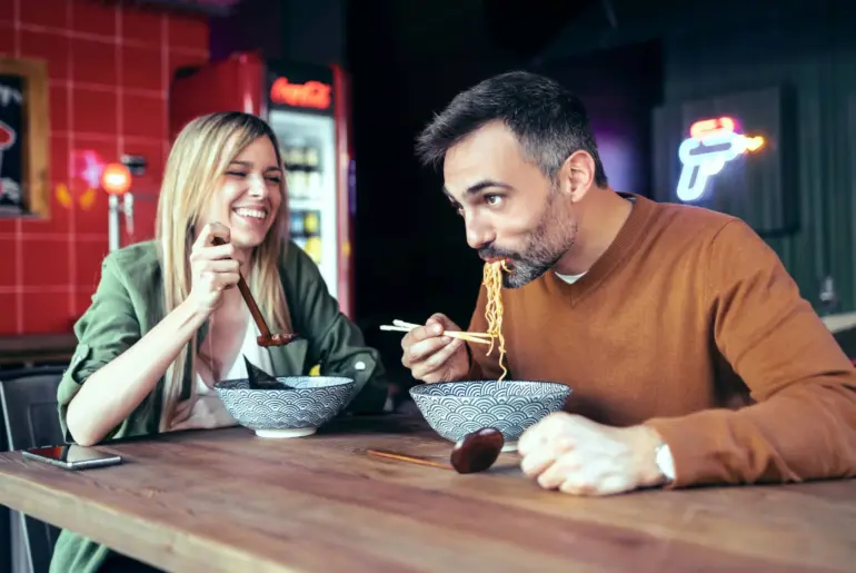 couple eating ramen with chopsticks while having fun in