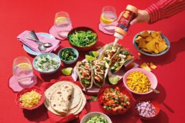 Laid table with tortillas, accompaniments and sauces on a red background
