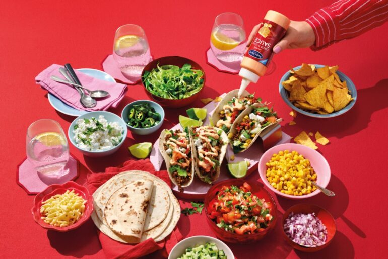 Laid table with tortillas, accompaniments and sauces on a red background